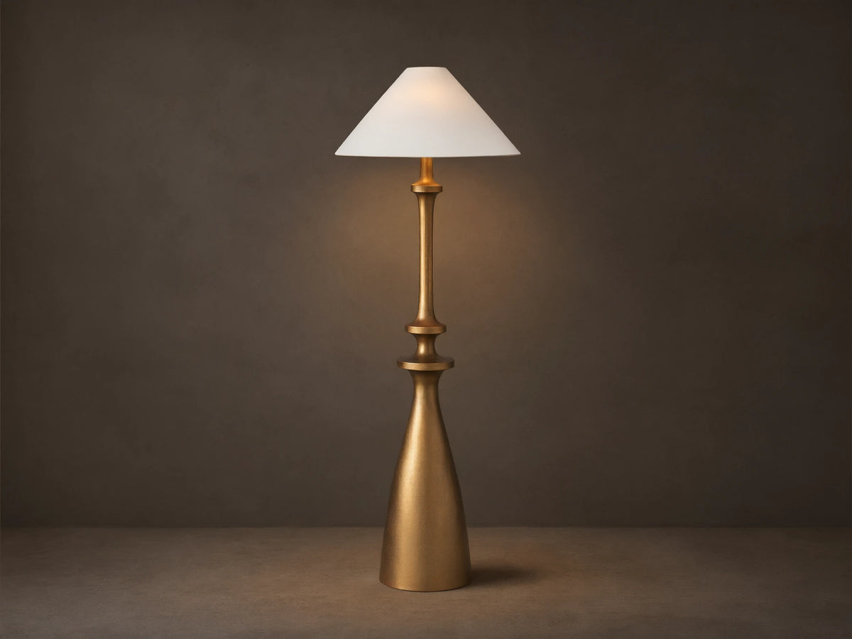 Murphy Floor Lamp with a brass-finished cast aluminum base and stem, topped with a white conical linen shade, standing on wood floor.