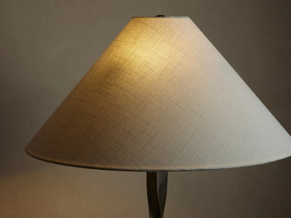 A floor lamp with a twisted dark metal base and a wide, white conical shade, positioned against a beige wall on wooden flooring.