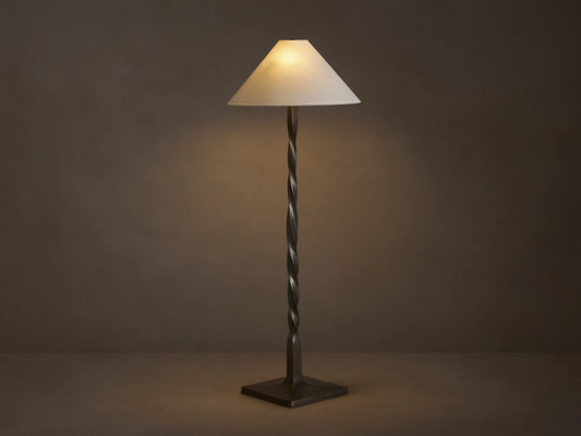 A tall floor lamp with a twisted bronze base and a conical cream lampshade, placed on a wooden floor against a neutral wall.