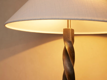 A twisted metal table lamp with a conical white shade on a wooden surface against a neutral wall background.
