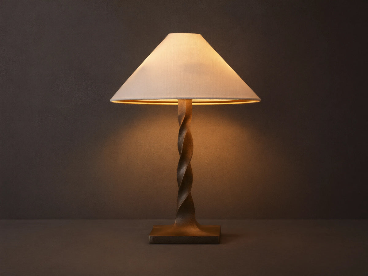 A table lamp with a twisted bronze base and a beige, conical fabric shade, casting a warm glow on a wooden surface.