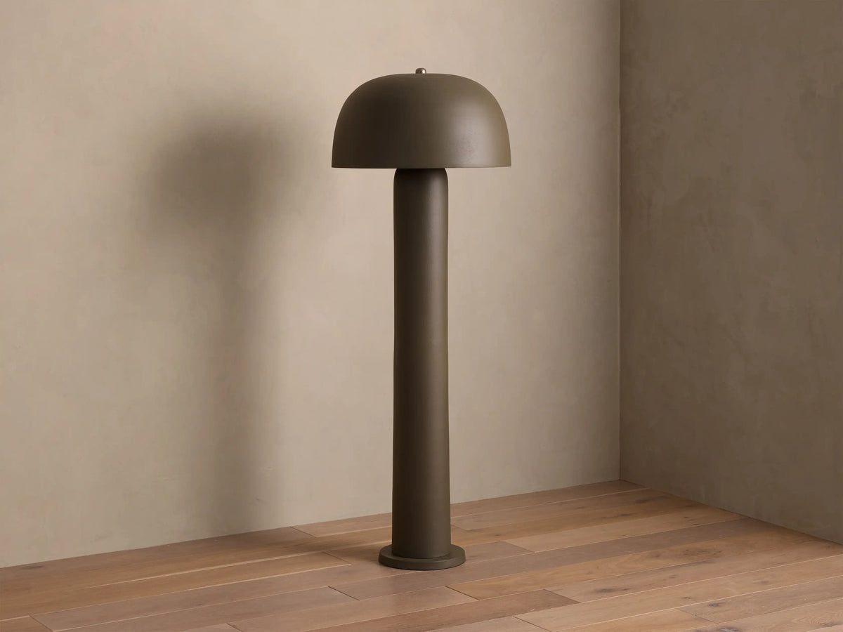 Dark olive green Mushroom Floor Lamp with a dome shade, casting a warm glow on a wall and wooden floor.