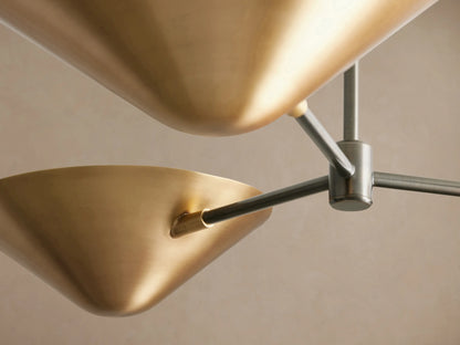 Simms Flush Mount ceiling light with three cone-shaped, polished brass shades and dark arms against a plain ceiling.