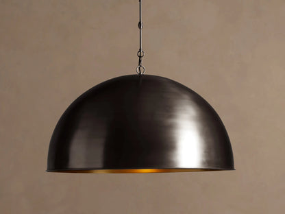 Watley Dome Pendant. Dark oxidized brass dome light, showing a gleaming golden interior, hanging against a brown wall.