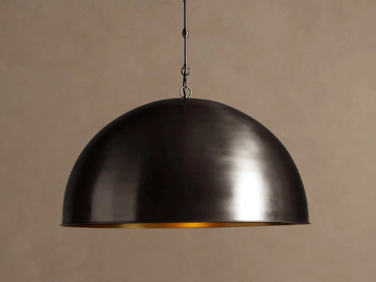 Watley Dome Pendant. Dark oxidized brass dome light, showing a gleaming golden interior, hanging against a brown wall.