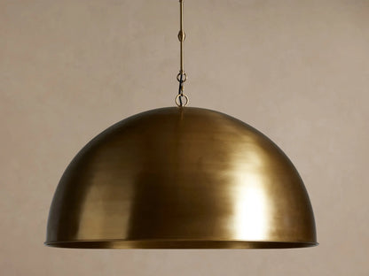 Watley Dome Pendant, antique brass dome-shaped light fixture hanging. Its interior shines with a warm, polished glow.