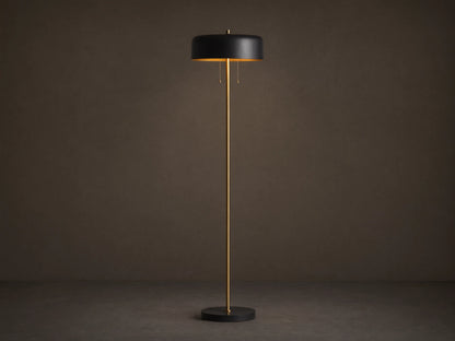 Oliver Floor Lamp: upright brass stem, black cylindrical shade with warm downward glow, black circular base on wooden floor.
