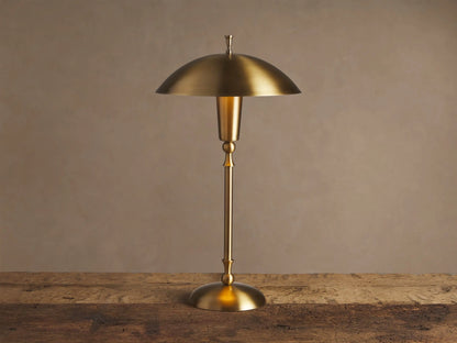 Archard Table Lamp with a lustrous brass finish, domed shade, and slender stem, standing on a rustic wooden surface.
