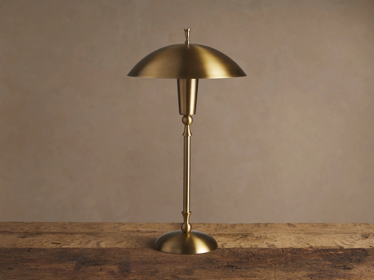 Archard Table Lamp with a lustrous brass finish, domed shade, and slender stem, standing on a rustic wooden surface.