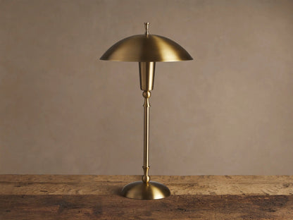 Archard Table Lamp with a lustrous brass finish, domed shade, and slender stem, standing on a rustic wooden surface.