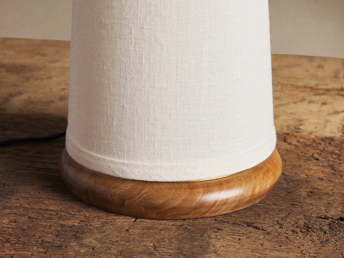 Close-up of Ombra Table Lamp's rounded teak wood base and cream linen shade, resting on a weathered wooden table.