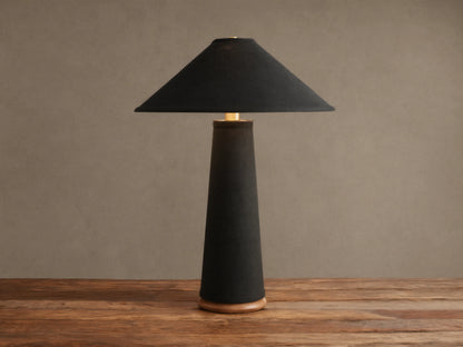 Ombra Table Lamp: Dark linen conical base & shade, teak wood base, antiqued brass accent, on rustic wood table.