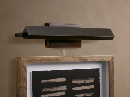 Zaeden Picture Light, angled dark bronze-plated iron fixture, mounted horizontally against a textured beige wall.