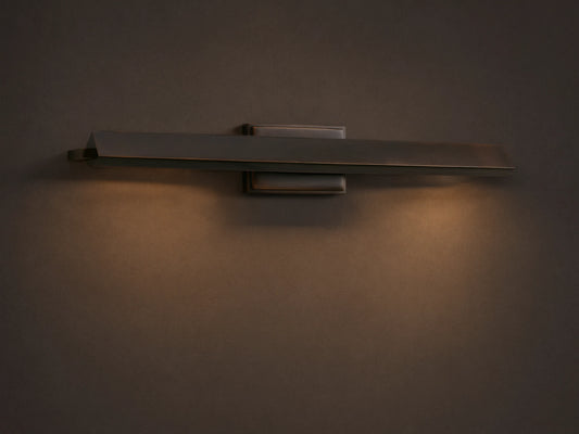 Zaeden Picture Light, horizontal bronze-plated iron fixture mounted on a light beige wall. It has a rectangular bar with an angled front.