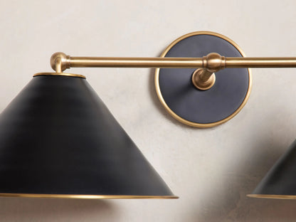 Matte black and brass Arno Double Sconce with conical shades and polished brass interior, mounted on a white wall.