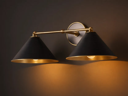 Arno Double Sconce with matte black cone-shaped shades, brass arm, polished brass interior, and round backplate on a wall.