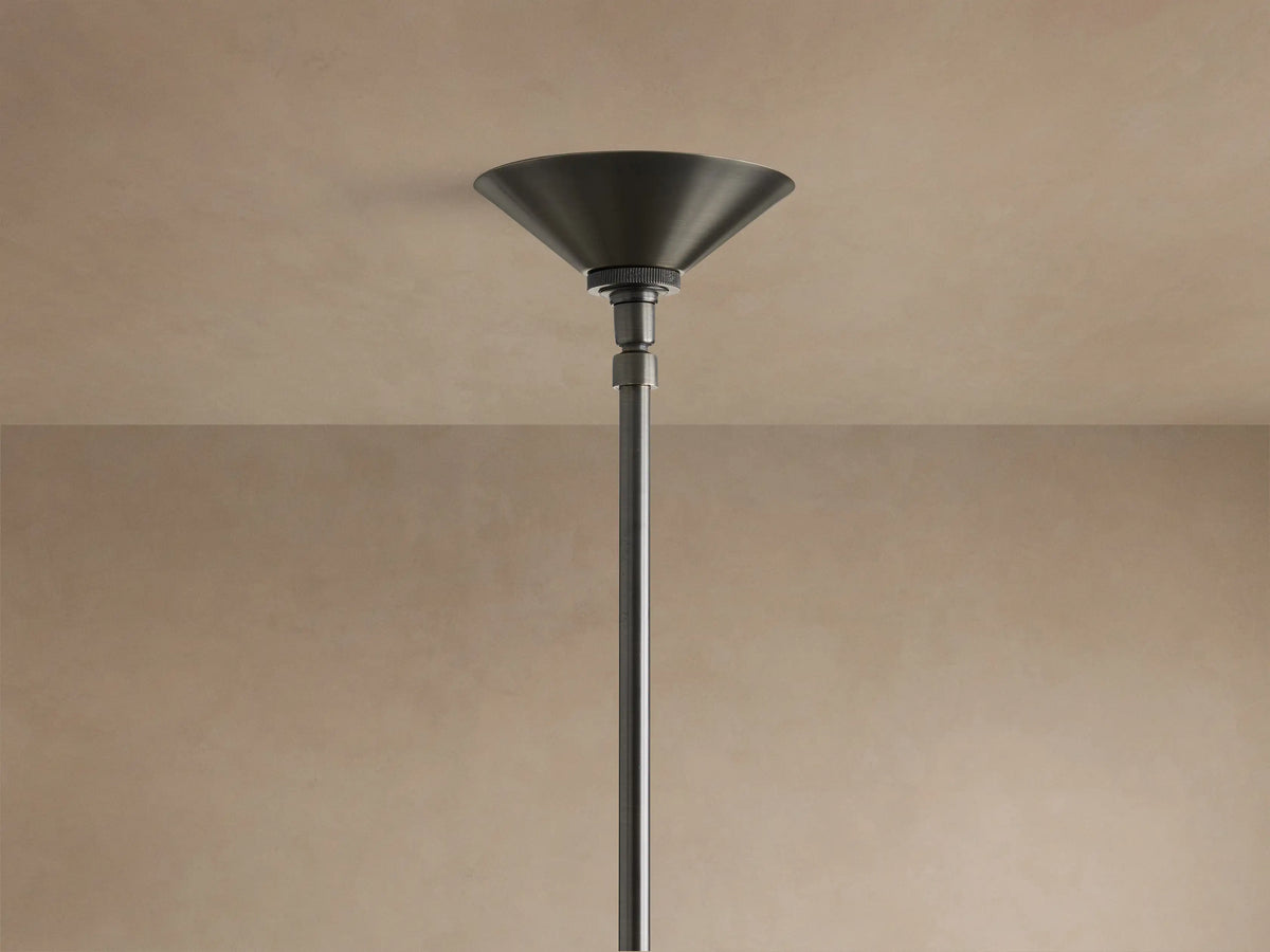 Simms Chandelier close-up: conical, antiqued brass shade illuminated by a warm bulb, with dark gray metal arms.