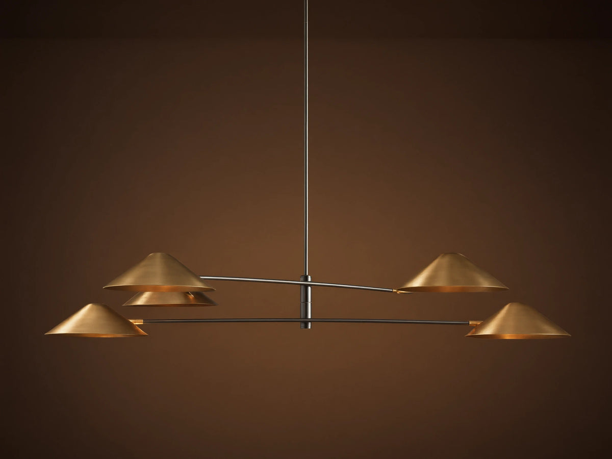 Simms Chandelier with four conical polished brass shades facing down, mounted on dark horizontal arms against a brown wall.