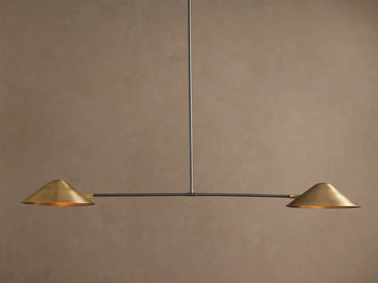 Simms Linear Chandelier with two downward-facing brass conical shades on a dark horizontal bar, suspended against a taupe wall.