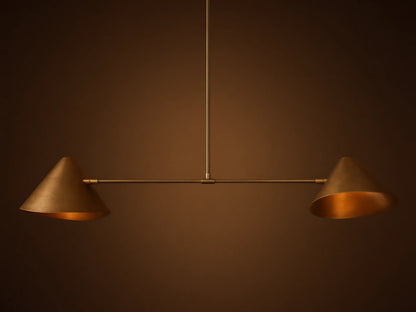 Simms Linear Chandelier with two downward-facing brass conical shades on a dark horizontal bar, suspended against a taupe wall.