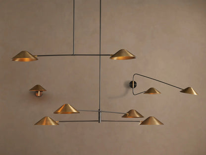 Simms Linear Chandelier. Modern fixture with two conical polished brass shades on a dark linear bar, suspended against a tan wall.