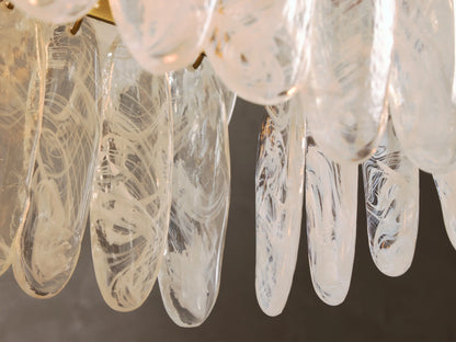 Close-up of clear glass art pieces with internal white swirled patterns, elongated and hanging vertically.