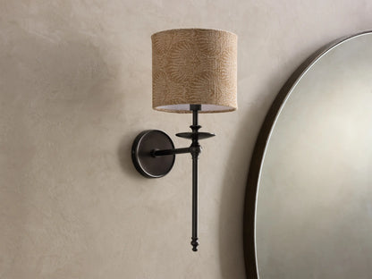 Close-up of a bronze Winslow Single Sconce with a lit, textured light brown fabric shade, mounted on a light wall.