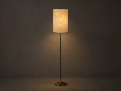 A tall, cylindrical floor lamp with a textured beige shade, emitting warm light. It has a slender black base, standing on a wooden floor.