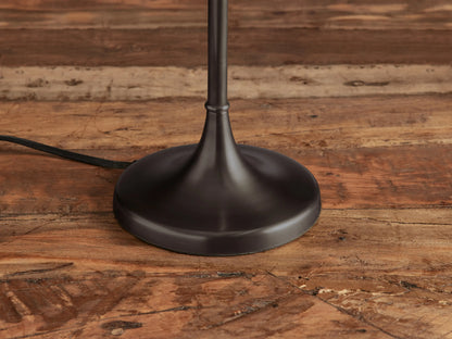 Lorelei Table Lamp with a tall white cylindrical shade, dark bronze slender stem & round base on a wooden table.