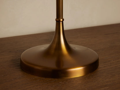 Lorelei Table Lamp, antique brass base & tall white linen shade, on wood, against a beige wall, with decor.