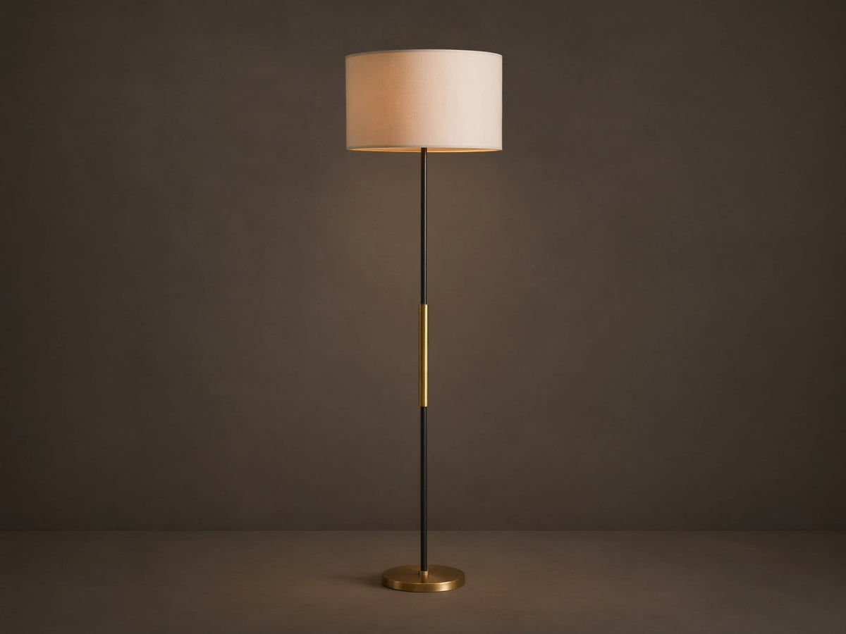 Ardea Floor Lamp with a matte black pole, antique brass detail, natural linen shade, and round brass base, against a neutral wall.