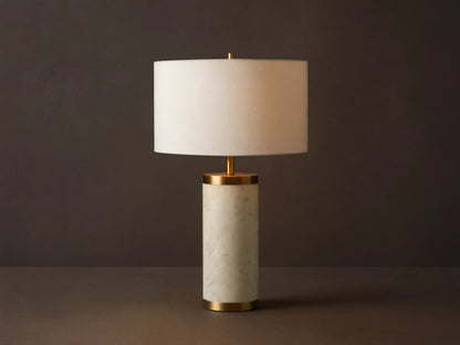 Caseti Table Lamp with ivory linen shade, cylindrical white marble base, and brass accents, on a wooden table.