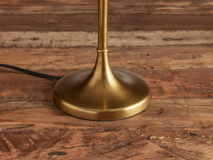 Lorelei Table Lamp, antique brass with a slender stand, round base, and a tall, cylindrical white linen shade, on wood.