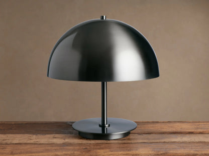 Malcom Table Lamp: dark brushed pewter dome shade, thin stem, and round base on a rustic wooden table.