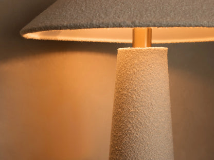 Close-up of a white bouclv©-textured base of a decorative object with a round wooden bottom on a wood table.