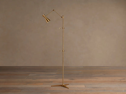 Tall, slender gold brass Jaxtyn Easel Floor Lamp with an angled light head, X-base, and small art display hooks.