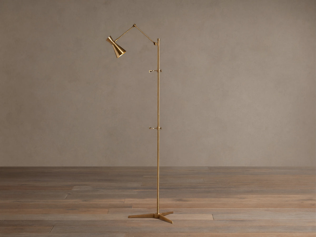 Tall, slender gold brass Jaxtyn Easel Floor Lamp with an angled light head, X-base, and small art display hooks.