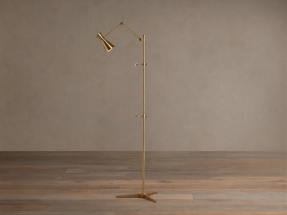 Tall, slender gold brass Jaxtyn Easel Floor Lamp with an angled light head, X-base, and small art display hooks.