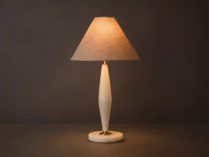 Front view of a lit table lamp with a conical beige fabric shade and a tapered creamy alabaster base with brass details.