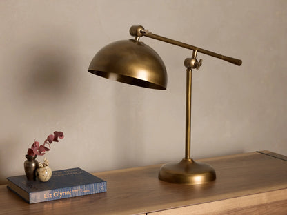 Front view of an antiqued brass industrial style desk lamp with an adjustable arm and dome shade, on a wooden surface.