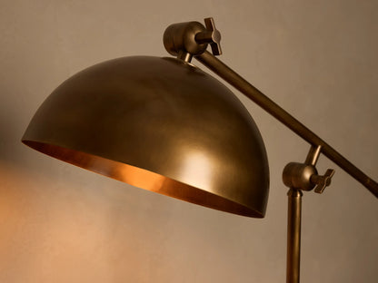 Front view of an illuminated brass industrial-style adjustable table lamp with a domed shade on a wooden surface.
