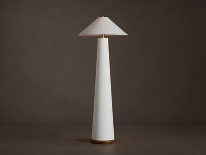 Ombra Floor Lamp: a tall white conical lamp with a white linen shade, teak base, and antiqued brass accents, on a wooden floor.