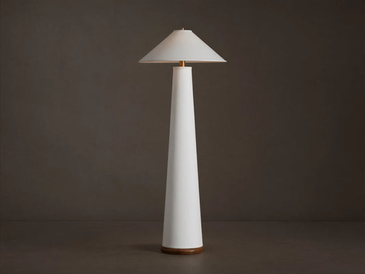 Ombra Floor Lamp: a tall white conical lamp with a white linen shade, teak base, and antiqued brass accents, on a wooden floor.