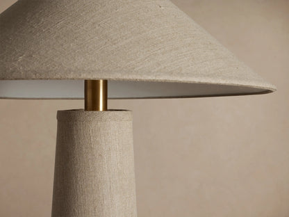 Ombra Floor Lamp, beige linen tapered column & conical shade, antiqued brass accent, teak wood base, on wood floor.