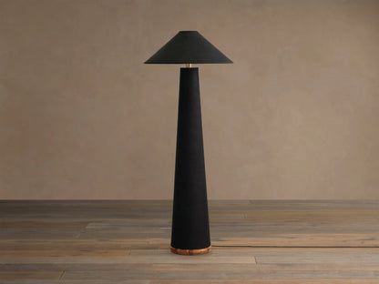 Ombra Floor Lamp. Tall, black linen-wrapped conical lamp with matching shade, brass top accent, and visible teak wood base. Emits warm light.