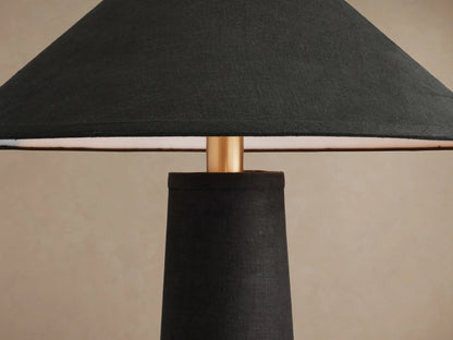 Ombra Floor Lamp, standing upright. Features a black conical linen shade and base, with antiqued brass and teak wood accents.