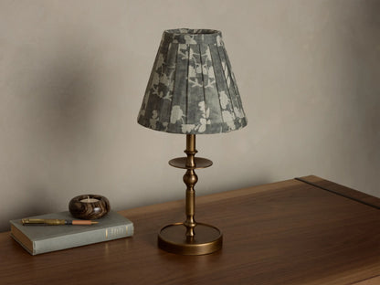 Front view of the Winslow Accent Table Lamp with an antique brass base and a pleated grey fabric shade with white floral pattern.