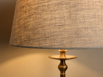Close-up of the Winslow Table Lamp, showing warm light from its charcoal fabric shade with visible weave, and antique brass base.