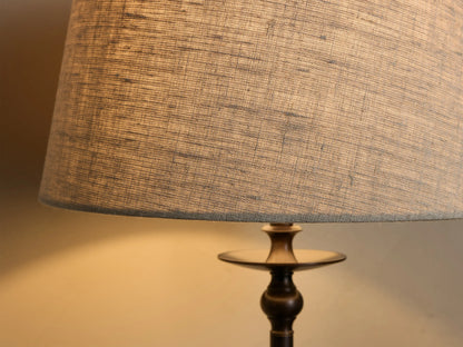 Front view of the Winslow Table Lamp, with a light natural fabric shade and dark bronze iron base, illuminated on a wooden table.