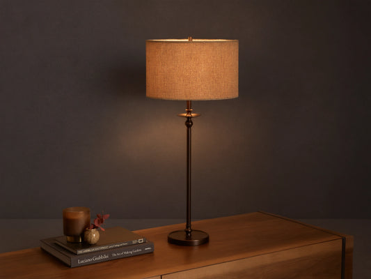 Illuminated Winslow Table Lamp with a bronze-finish iron base and a light brown patterned fabric drum shade on a wooden surface.